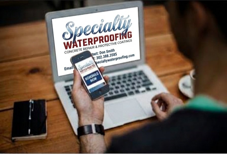 Person holding a smartphone in front of a laptop displaying a Specialty Waterproofing concrete repair and protective coatings advertisement.