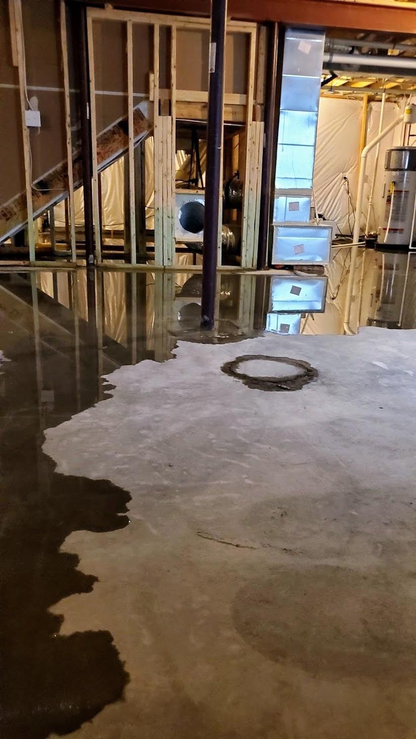 Basement with standing water on a concrete floor, exposed wall framing, pipes, and HVAC equipment.