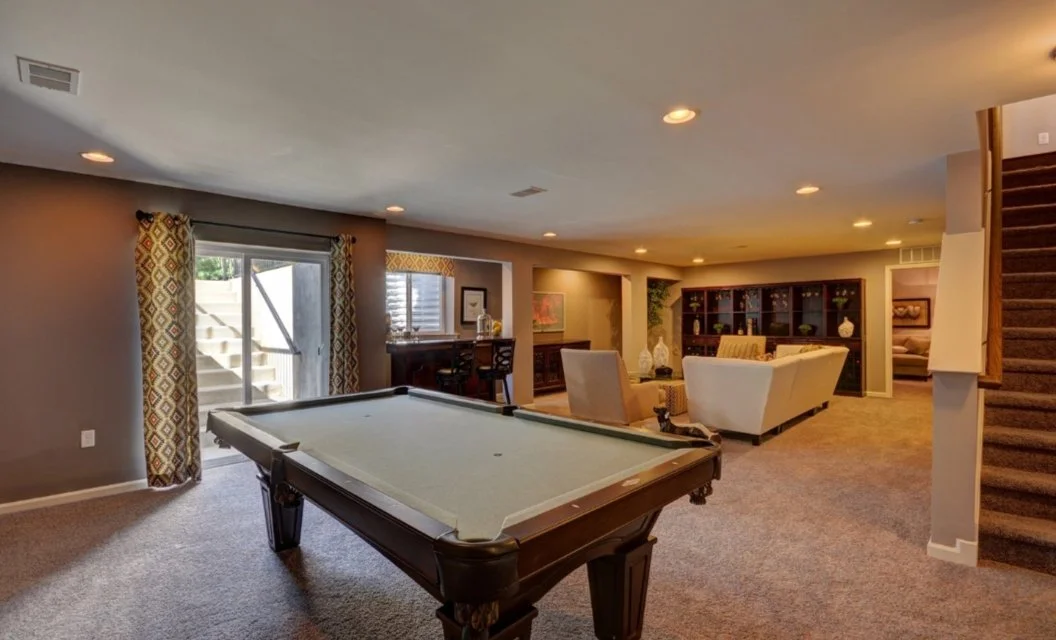 Beautiful finished basement with pool table, sectional seating, wet bar, display cabinet, sliding glass door, and carpeted staircase