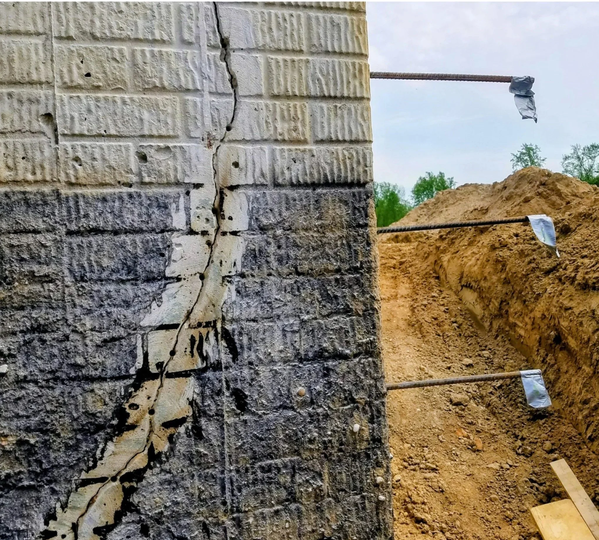 Cracked concrete poured foundation wall reinforced with steel rebar beside an excavated dirt trench