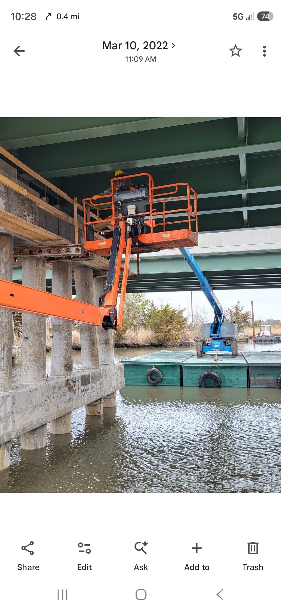 Orange and blue boom lifts on a barge beneath a bridge over a waterway.