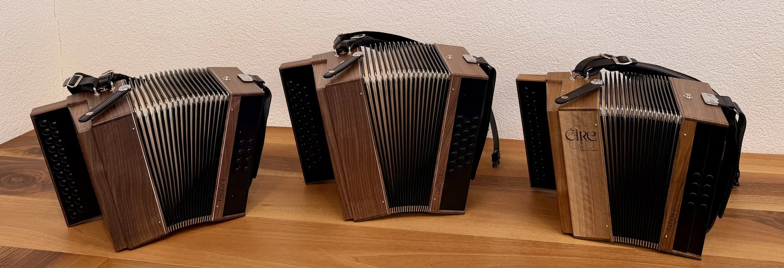 Drei hölzerne Knopfakkordeons mit ausgezogenen Bälgen auf einem Holztisch