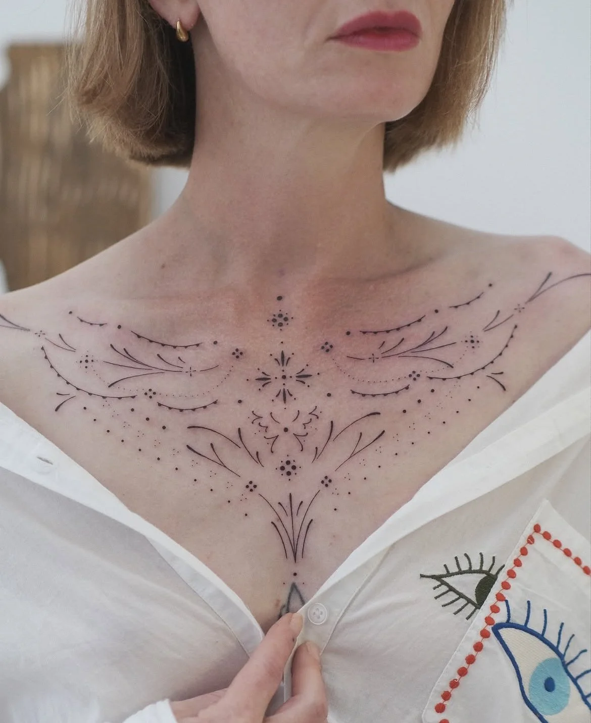 Gros plan sur une femme portant un tatouage floral et géométrique délicat sur le haut de la poitrine.