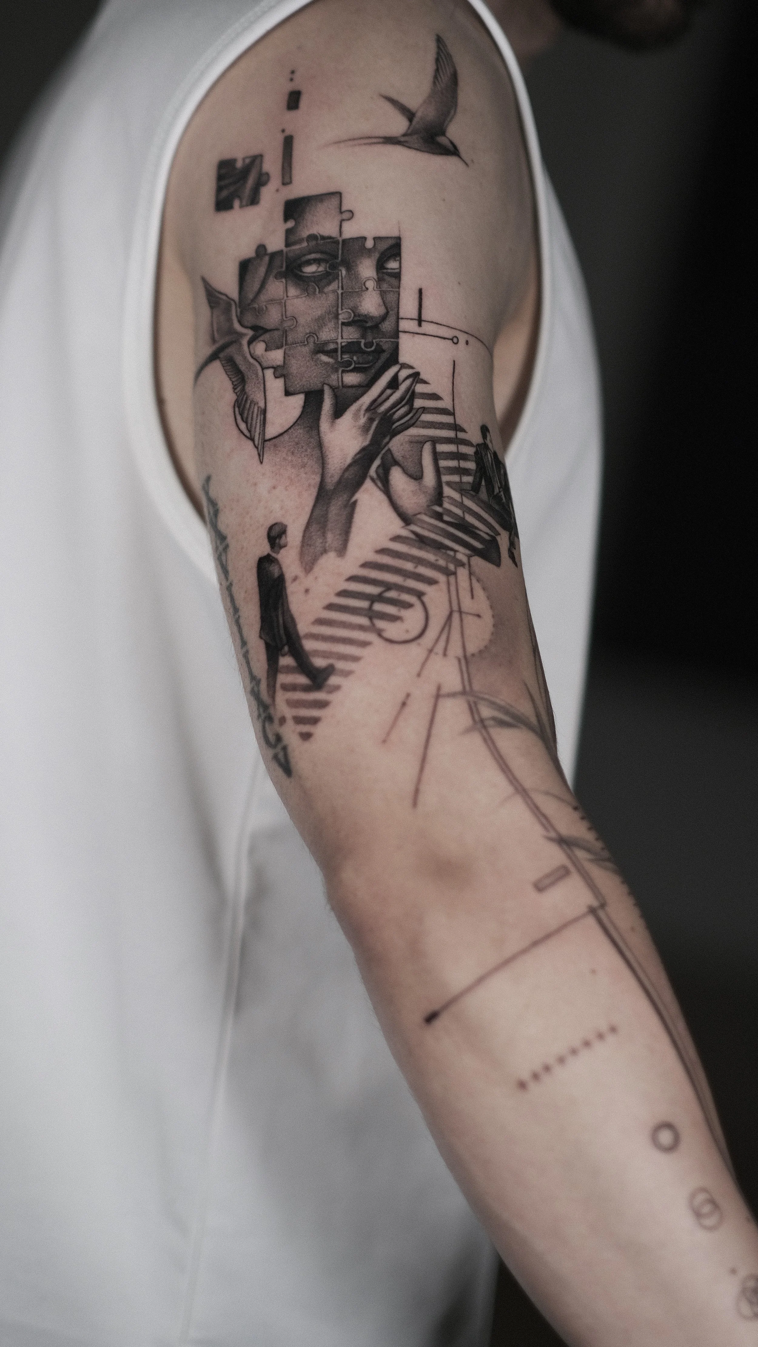 Gros plan d’un tatouage réaliste représentant un visage fragmenté en pièces de puzzle sur un bras.
