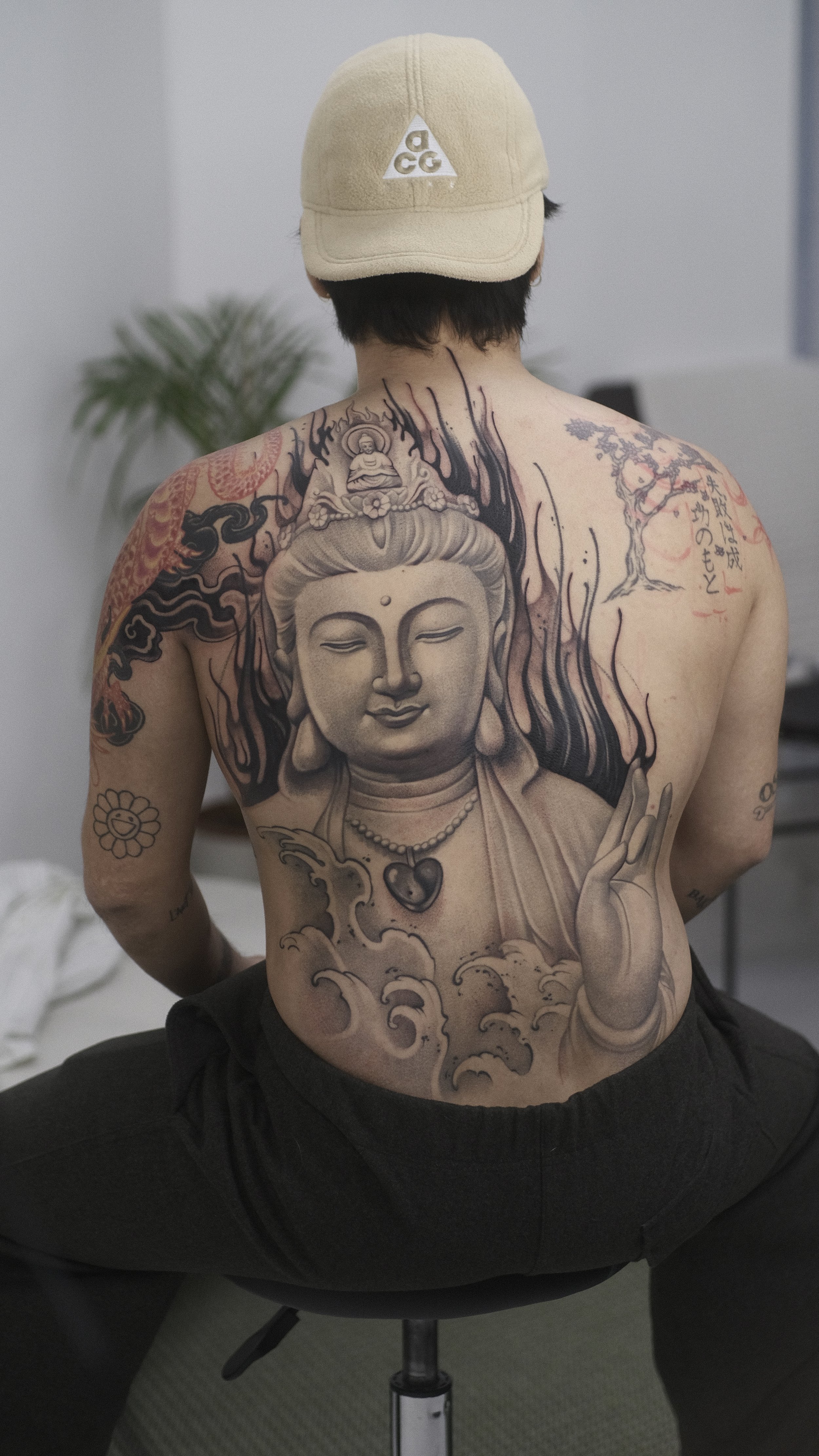 Personne tatouée portant une casquette beige, avec un grand tatouage de Bouddha sur le torse