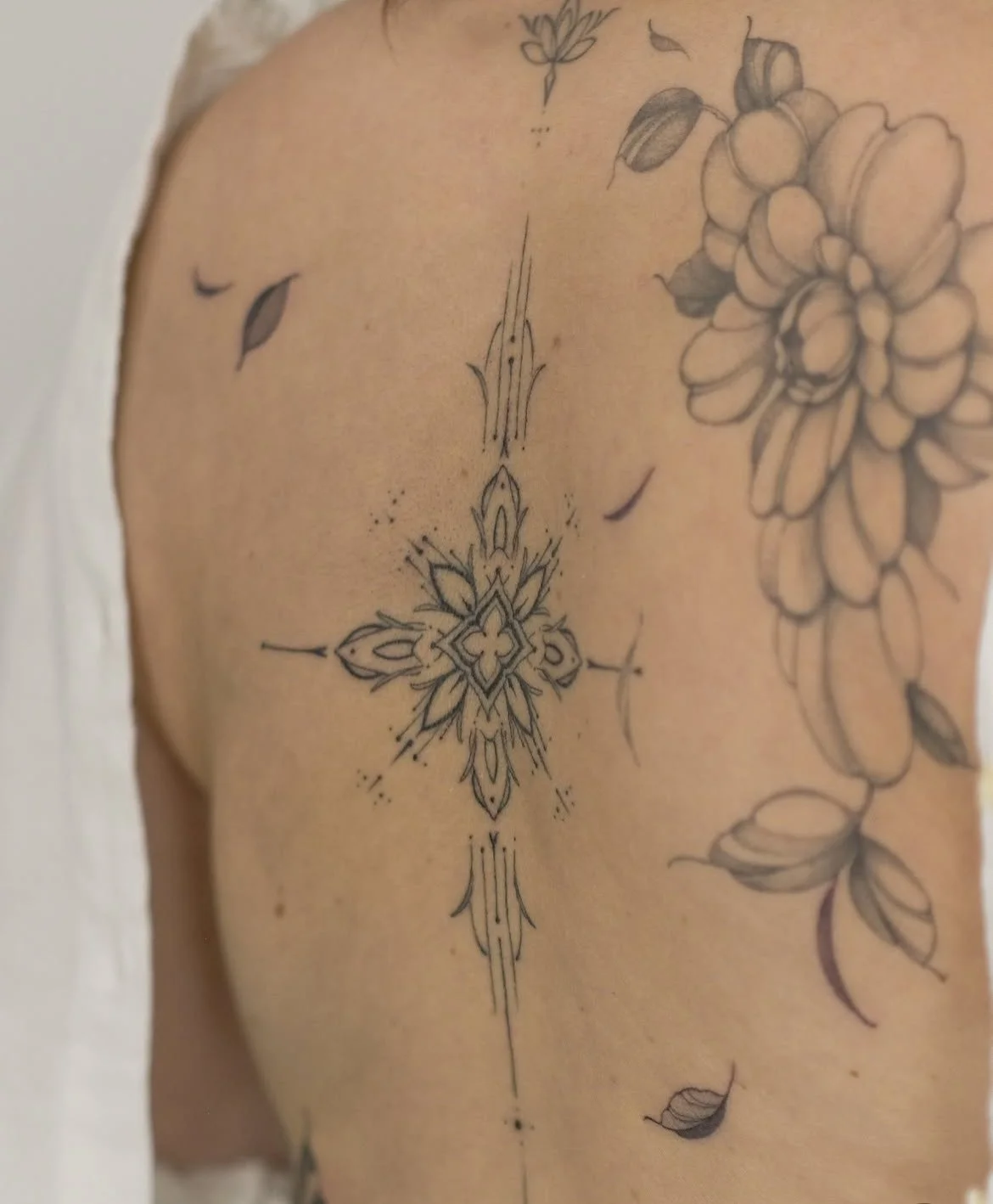 Gros plan sur un tatouage ornemental géométrique entouré de fleurs et de feuilles sur le haut du bras.