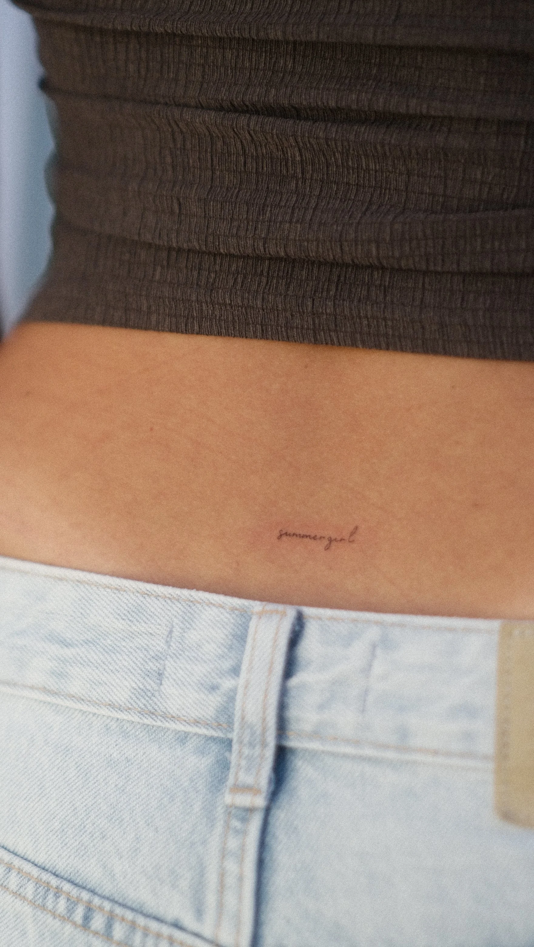 Gros plan d’un tatouage manuscrit sur une peau, au-dessus d’un jean clair et d’un vêtement sombre.