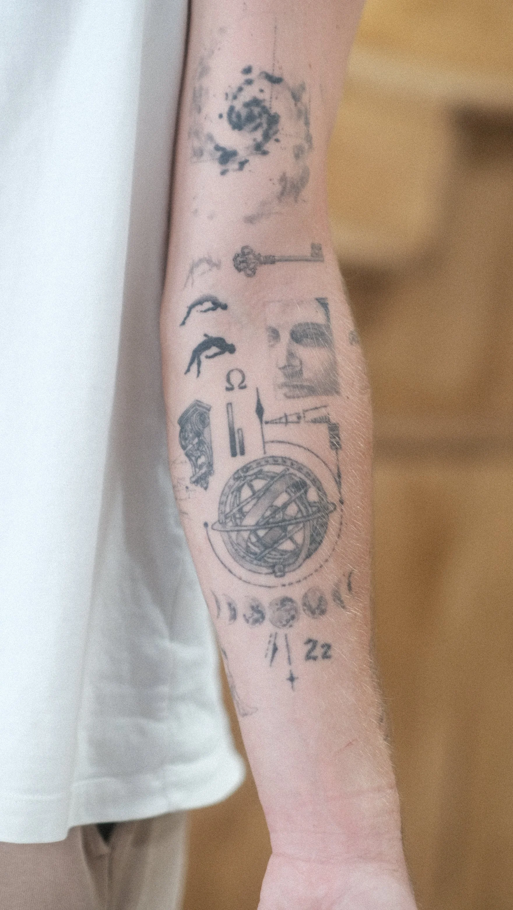 Gros plan d’un avant-bras couvert de tatouages représentant une clé, des symboles et une sphère armillaire.