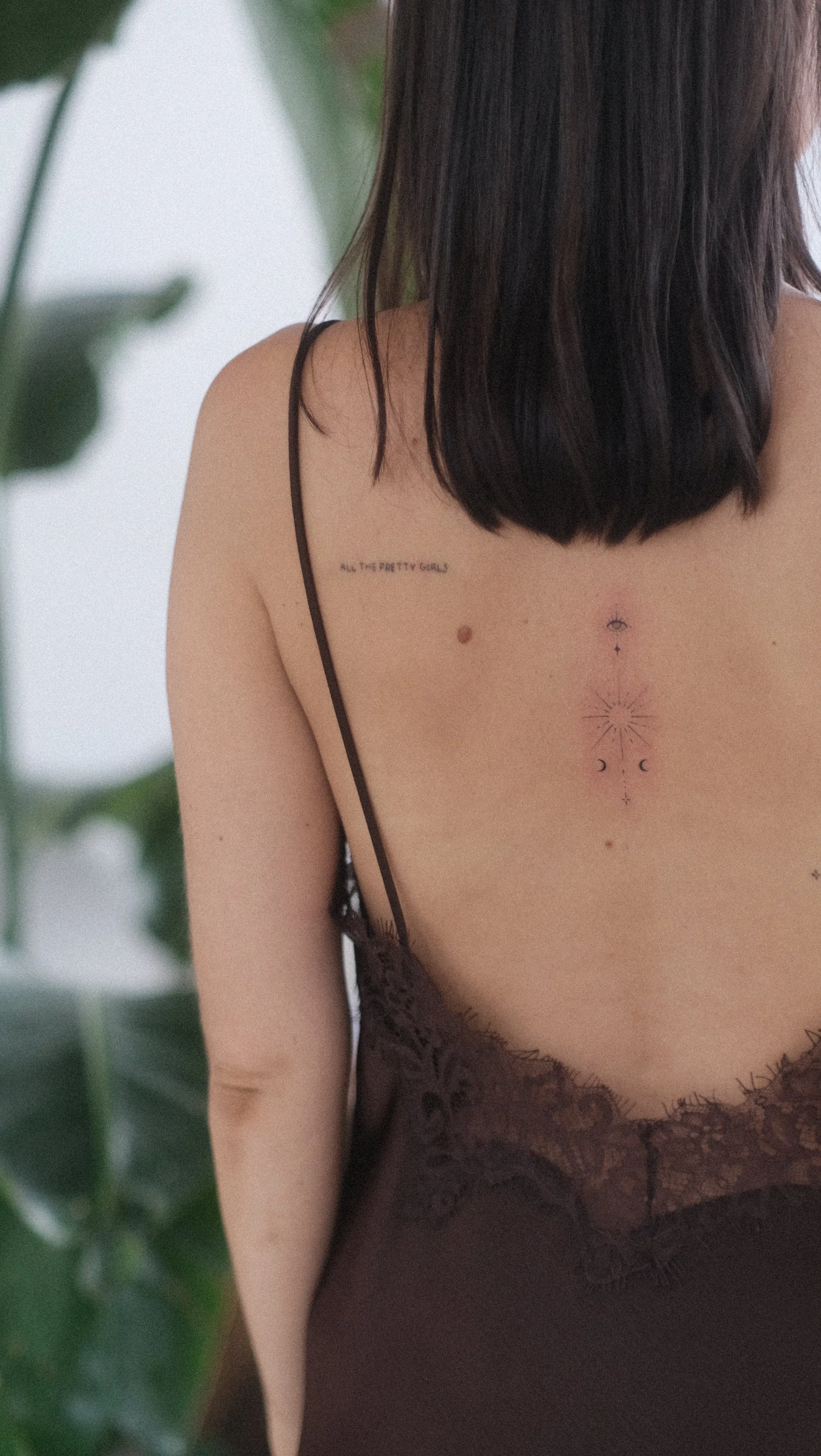 Dos d’une femme aux longs cheveux noirs portant une nuisette en dentelle, avec des tatouages visibles sur le dos.