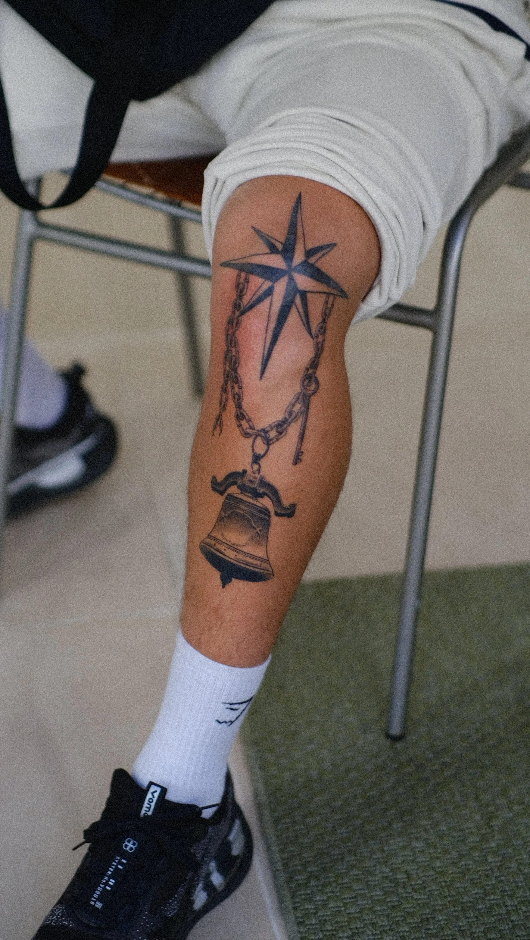 Gros plan d’une jambe tatouée d’une étoile nautique, d’une chaîne et d’une ancre, portant une chaussette blanche et une chaussure noire.