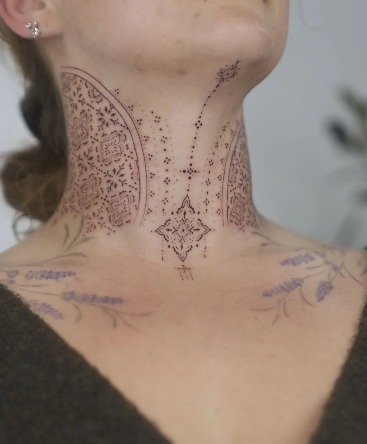 Gros plan du cou et du haut du dos d’une personne portant un tatouage ornemental fin aux motifs floraux et géométriques.
