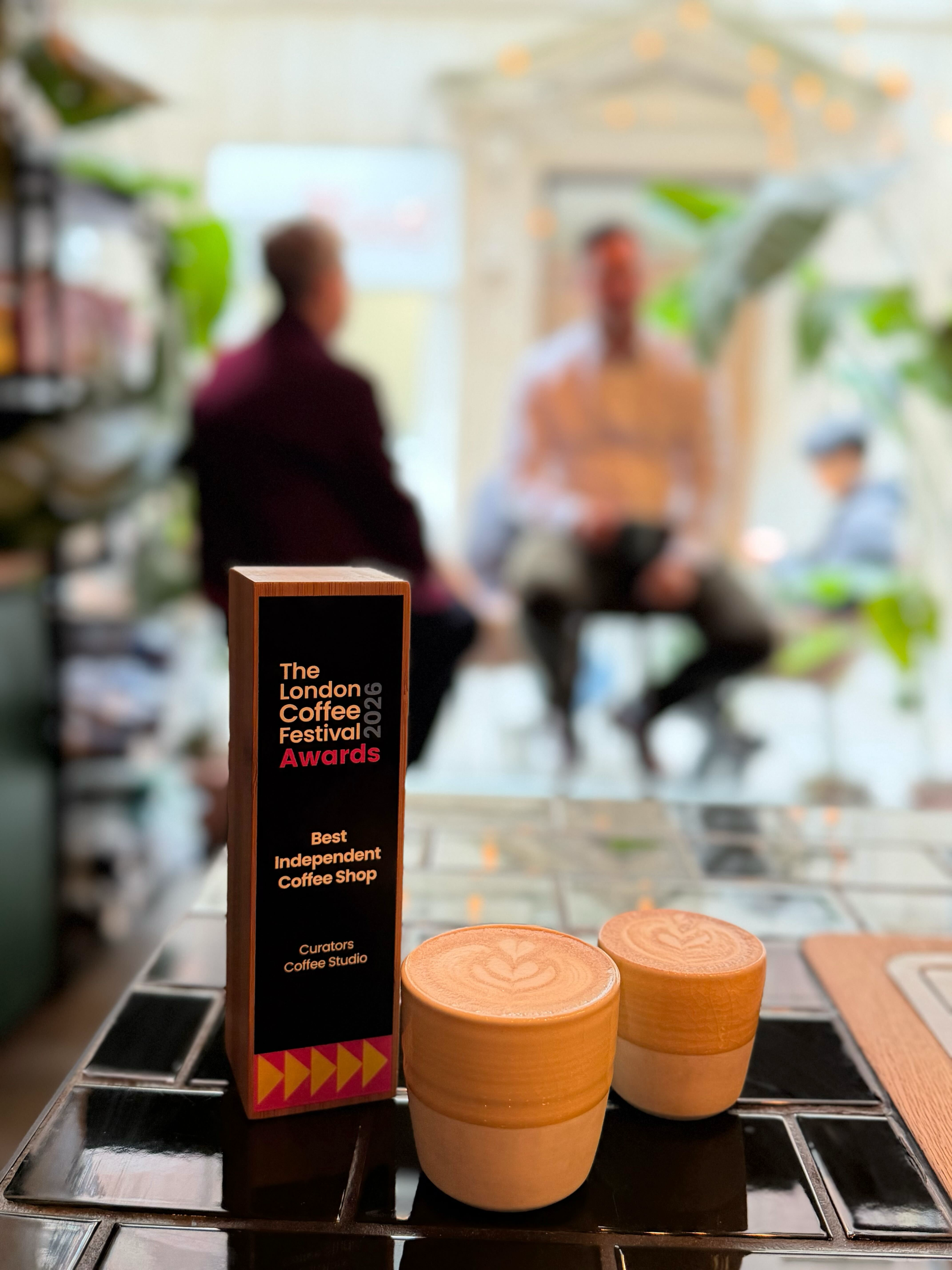 Two latte art coffees beside a London Coffee Festival 2026 Awards trophy for Best Independent Coffee Shop.