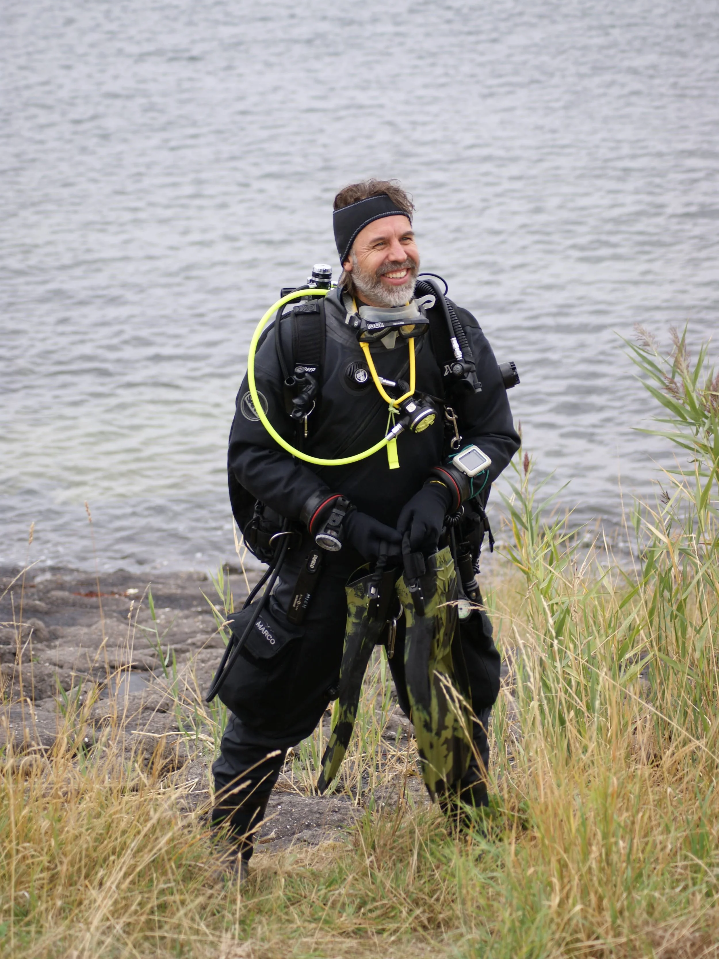 Smiling scuba diver in full gear standing beside a lake in tall grass