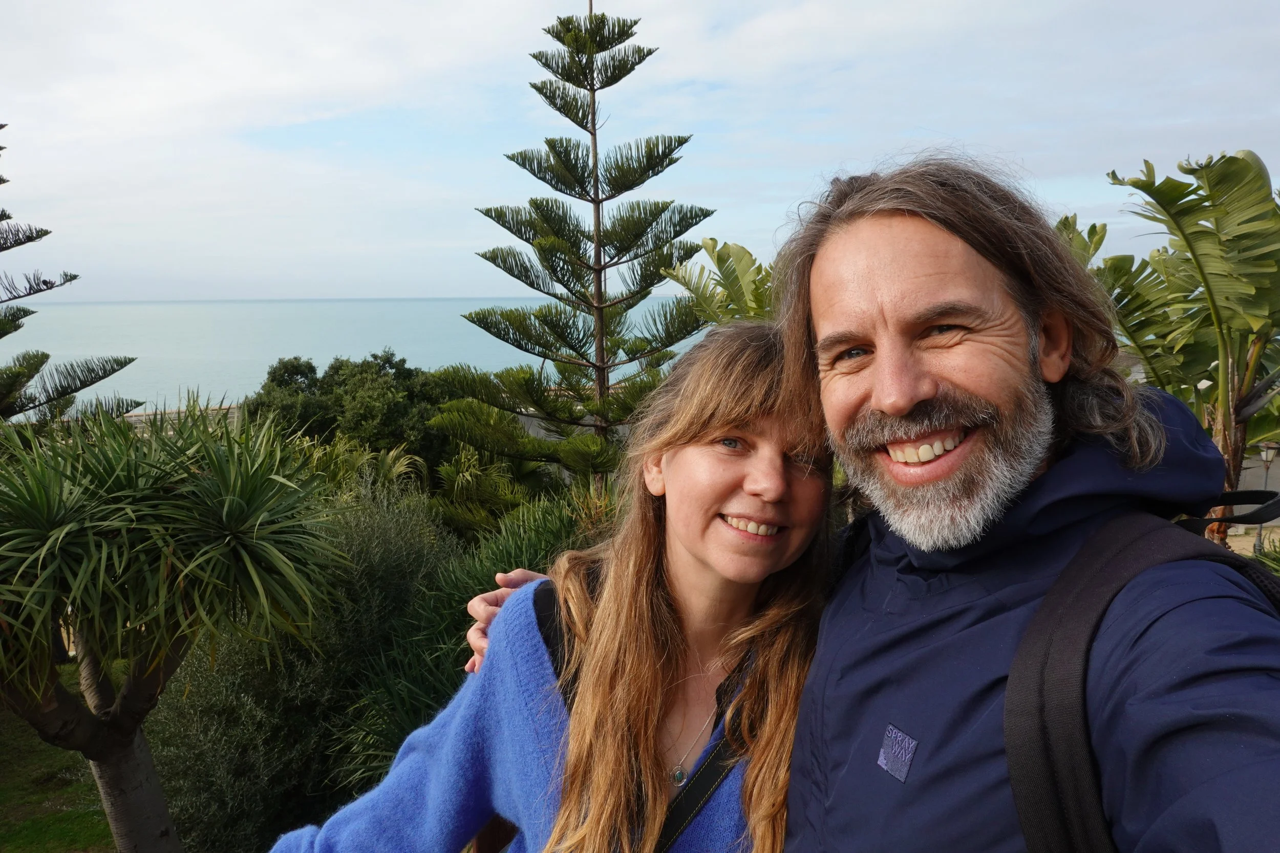 Smiling couple taking a selfie in a lush seaside garden with tropical plants and ocean views