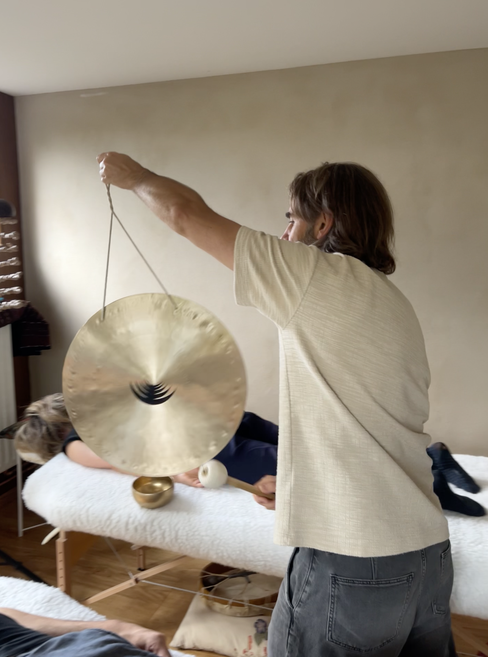 Person playing a large hanging gong during a sound bath session in a room