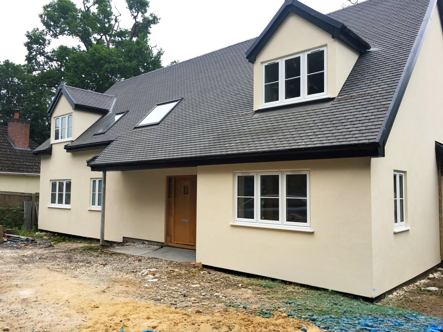 Newly built cream-colored suburban house with a grey slate roof, dormer windows, skylights, and unfinished landscaping