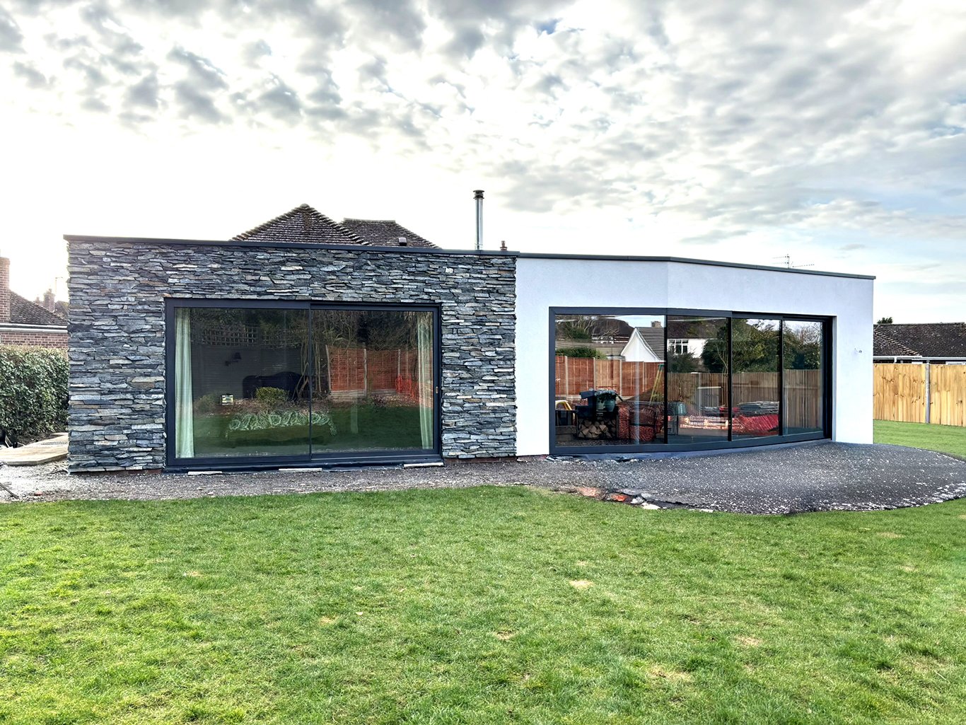 Modern home extension with slate stone walls, white exterior, large glass sliding doors, and a grass lawn