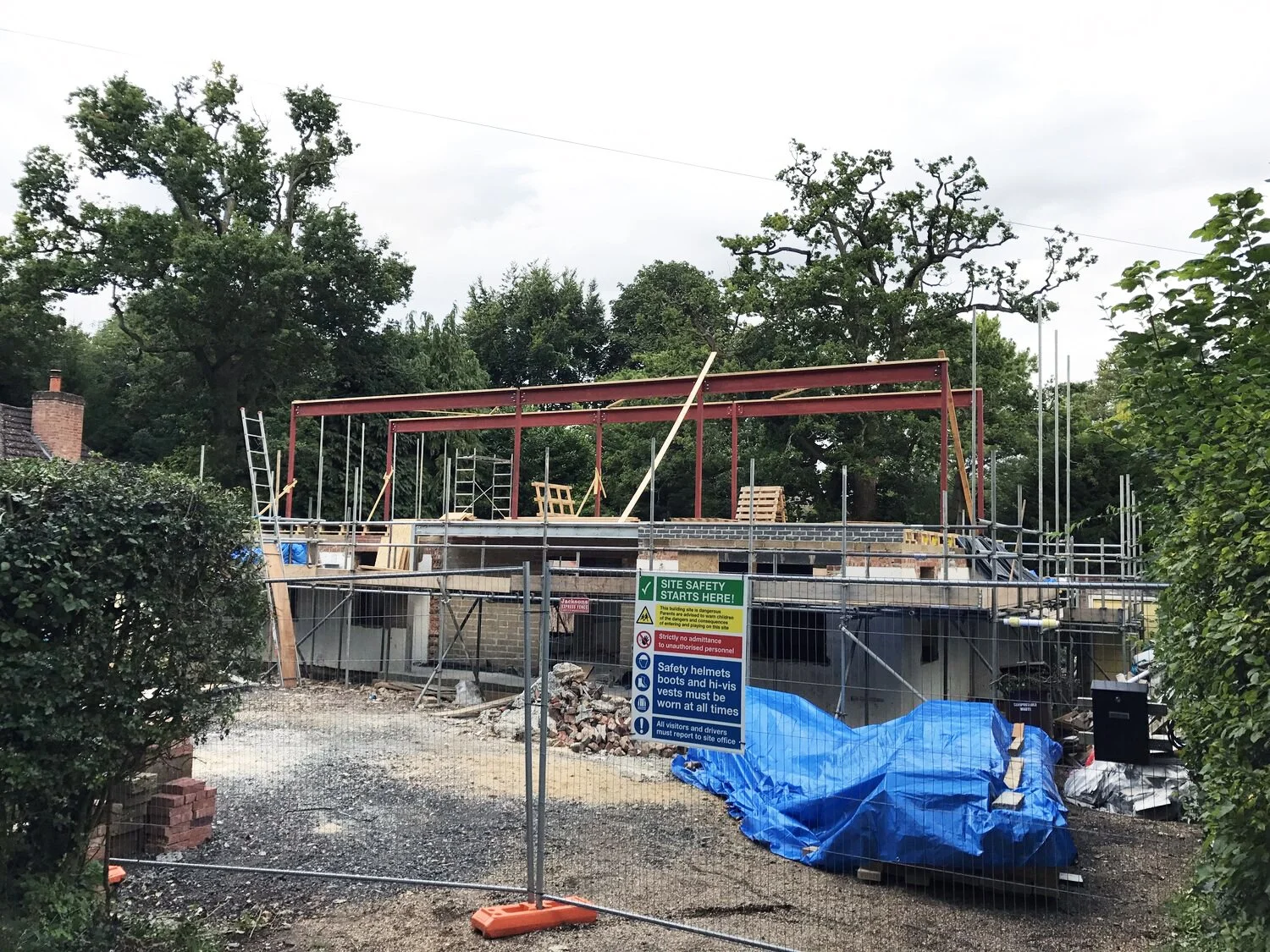 Residential construction site with steel framing, scaffolding, safety fencing, and a site safety sign