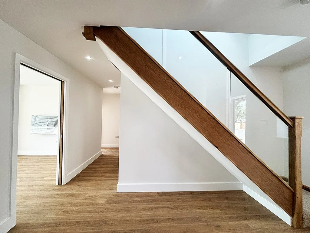 Modern home hallway with wood flooring, white walls, and a staircase featuring wood railings and glass panels