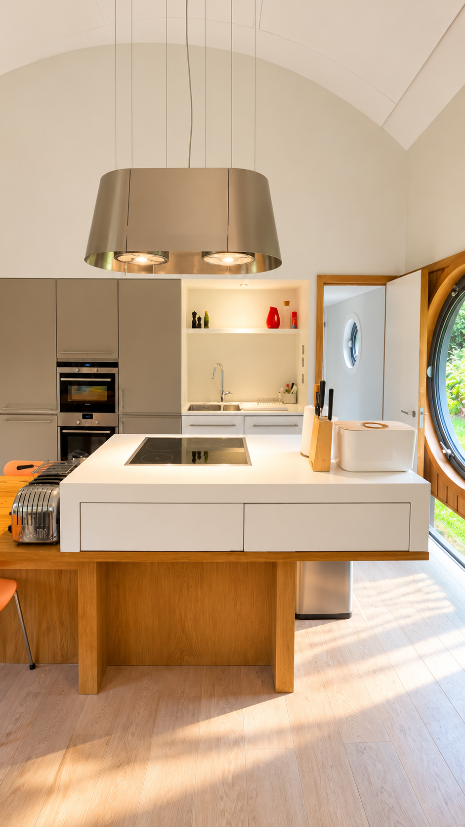 Modern kitchen with white island, induction cooktop, stainless steel appliances, pendant light, and round wood-framed window