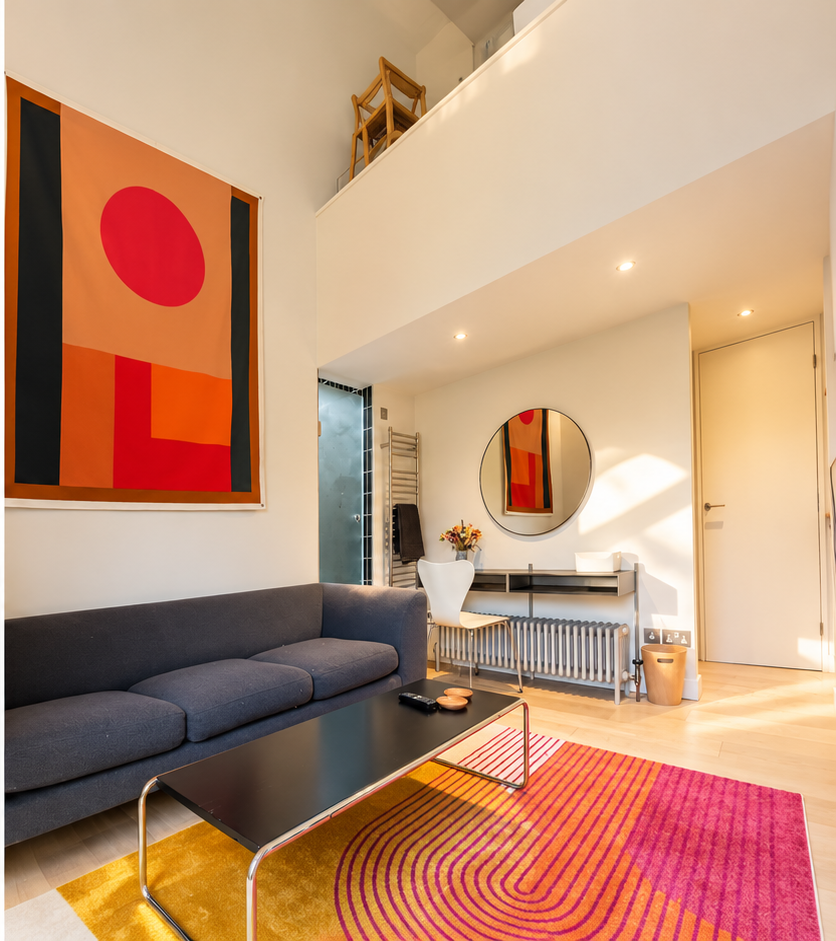 Modern living room with dark sofa, black coffee table, colorful geometric rug, abstract wall art, round mirror, and mezzanine