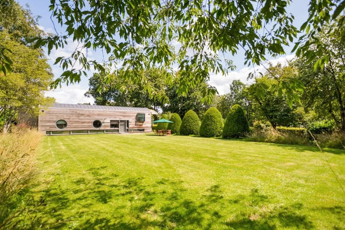 Modern wooden cabin with round windows in a manicured garden surrounded by trees