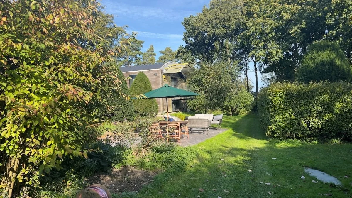 Landscaped backyard garden with a modern house, patio furniture, and a green market umbrella on a sunny day