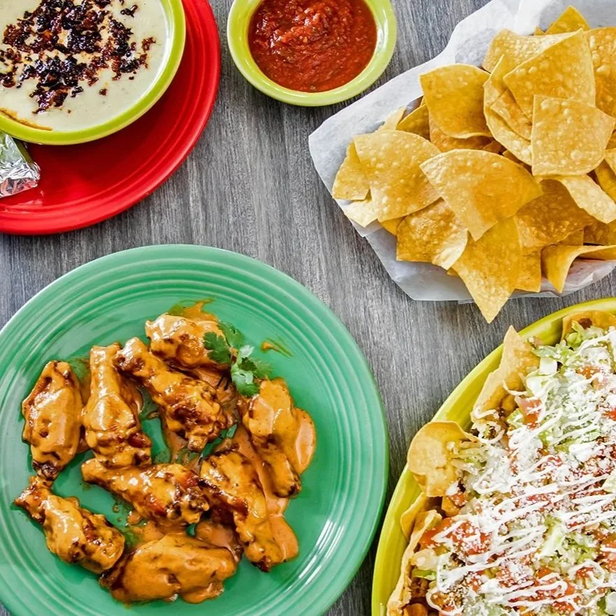 Mexican food spread with tortilla chips, salsa, queso dip, saucy grilled chicken, and a loaded taco salad.