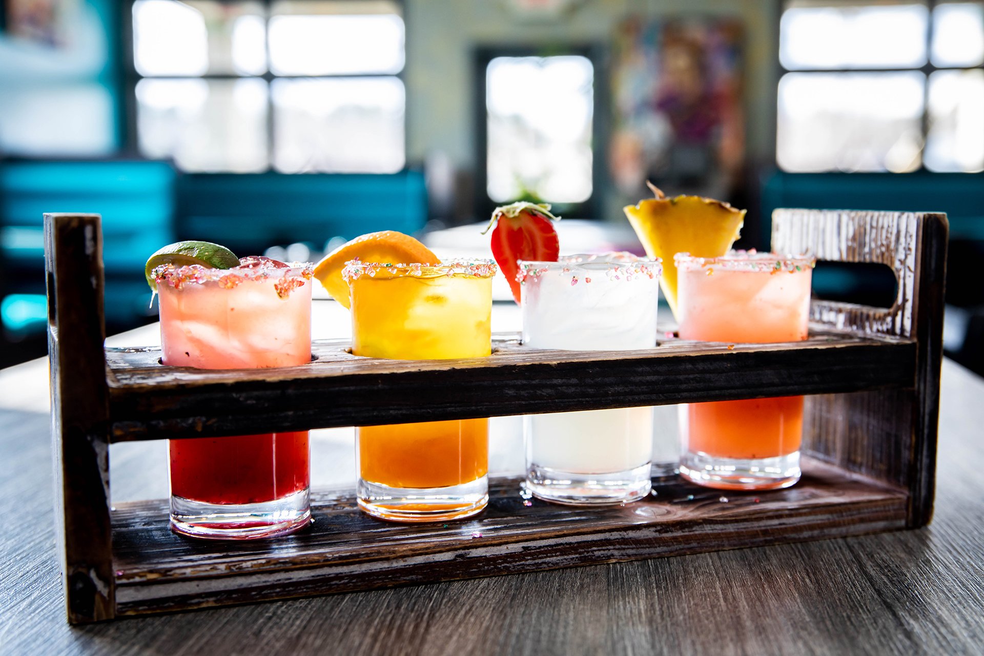 Five colorful fruit cocktails with sugared rims on a two-tier wooden serving tray