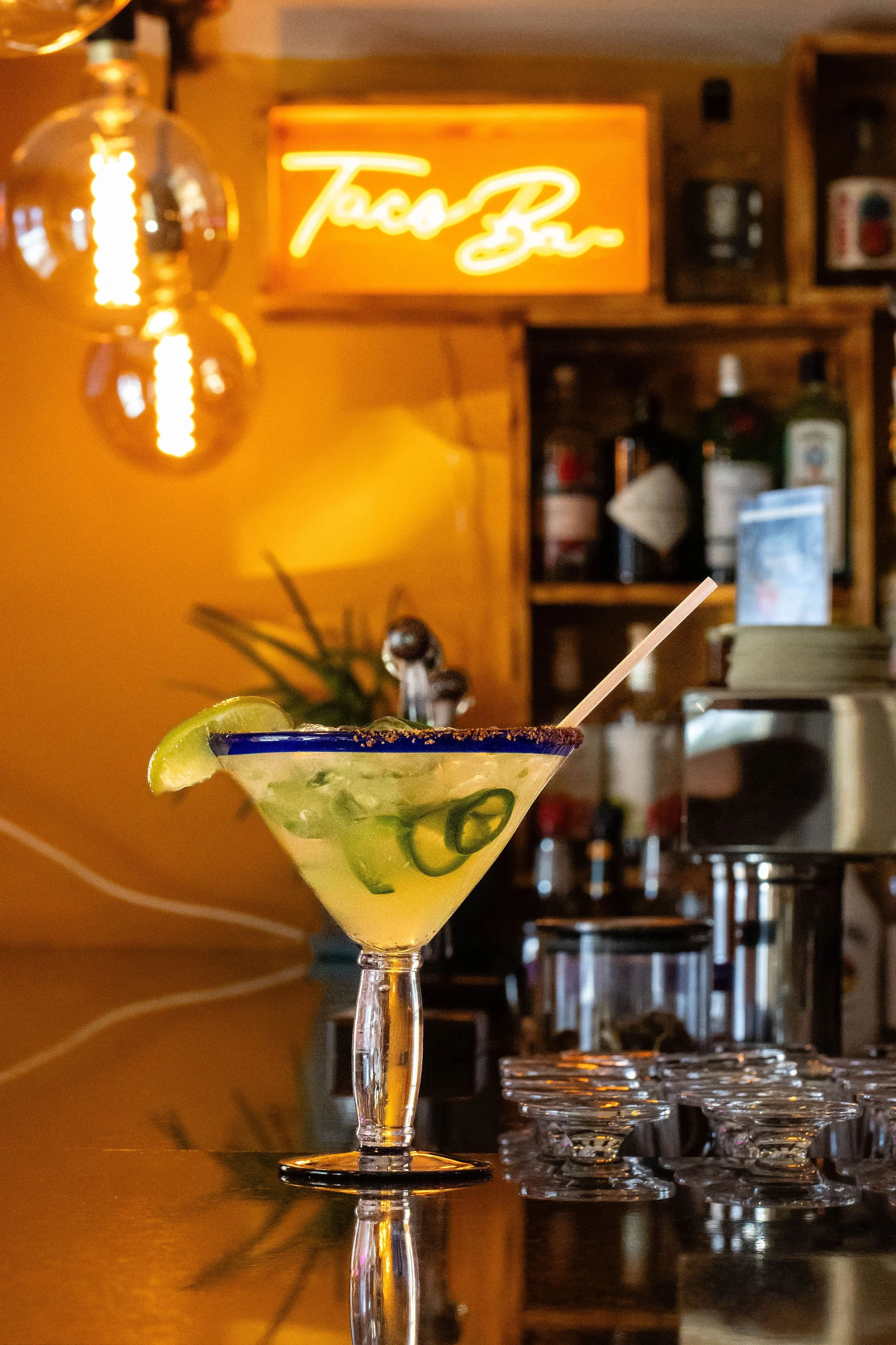 Margarita with lime garnish and chili-salt rim on a bar counter in a warmly lit restaurant