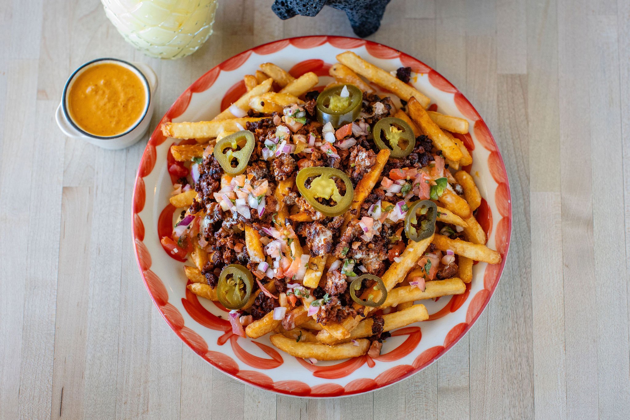 Loaded fries topped with seasoned ground beef, pico de gallo, white sauce, and sliced jalapeños, served with cheese dipping sauce