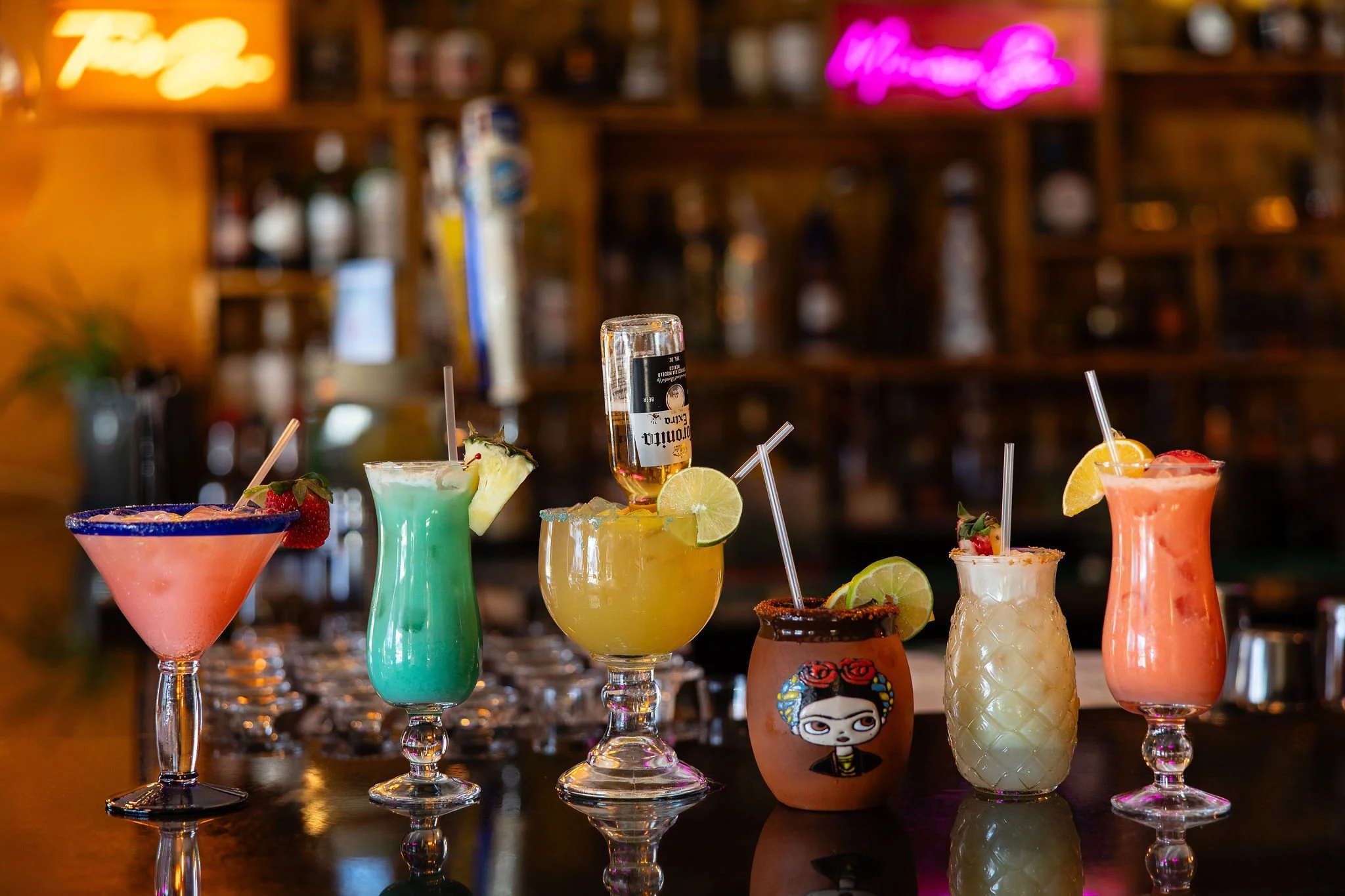 Colorful cocktails with fruit garnishes and straws displayed on a bar counter.