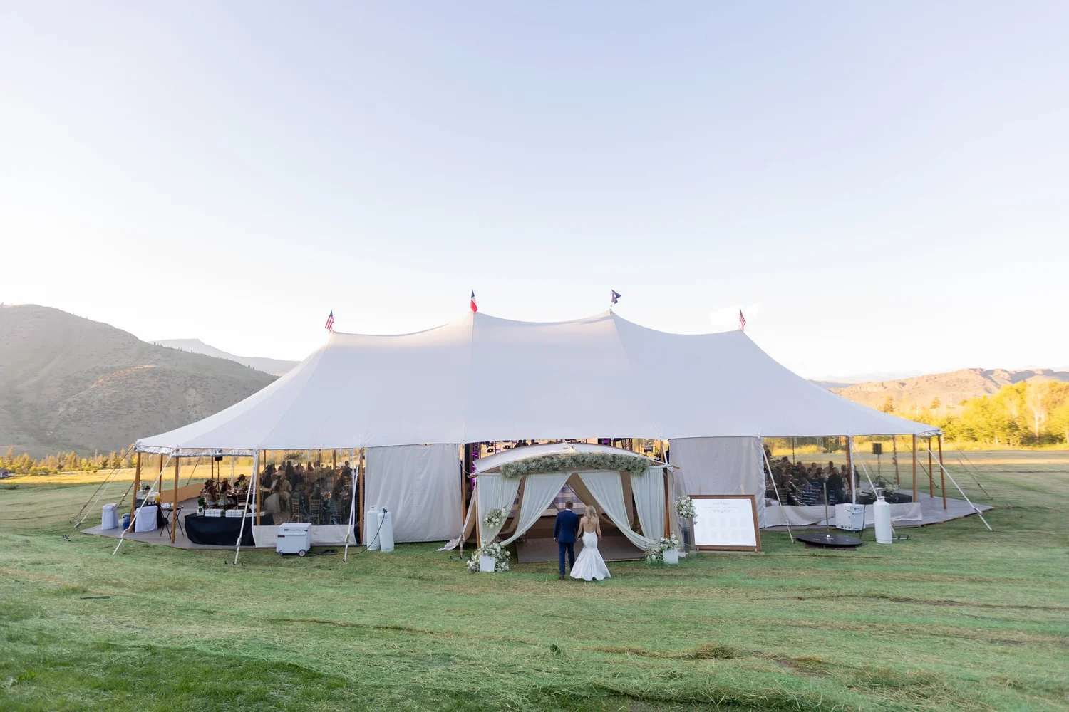 Large white stretch tent set on a green meadow with mountains behind at Tundra Springs, Colorado mountain wedding venue