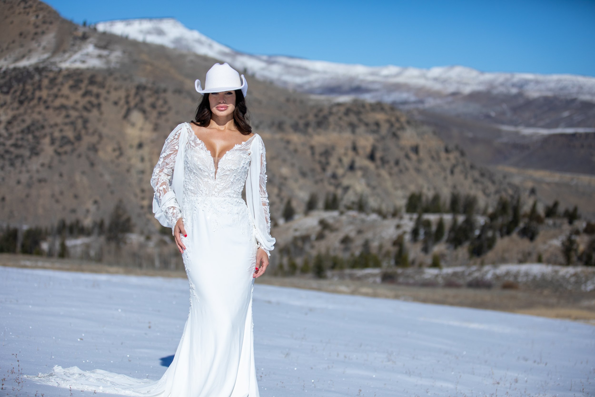 Bride in a lace gown with a sweeping train on a snowy hillside at Tundra Springs, Colorado mountain wedding venue