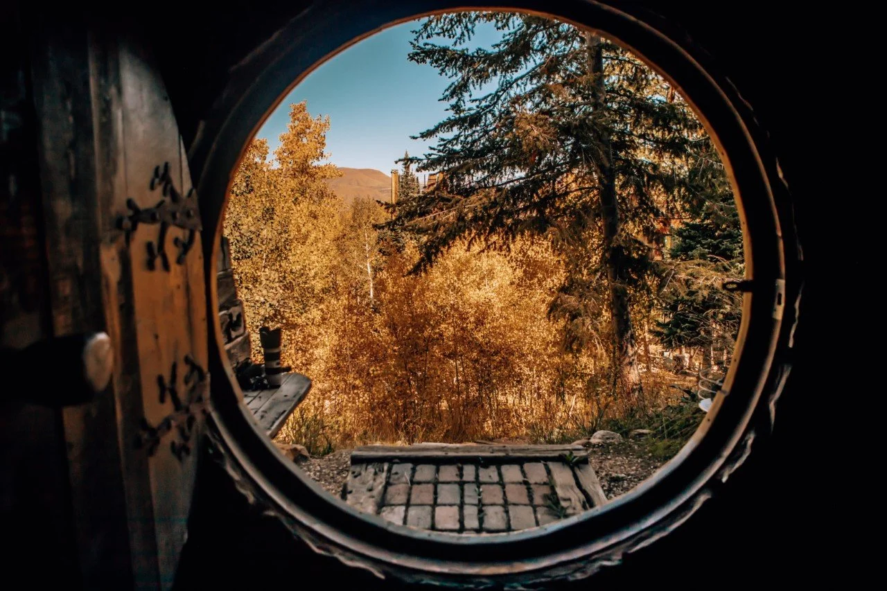 View through a round porthole window framing golden aspens at Tundra Springs, Colorado mountain wedding venue