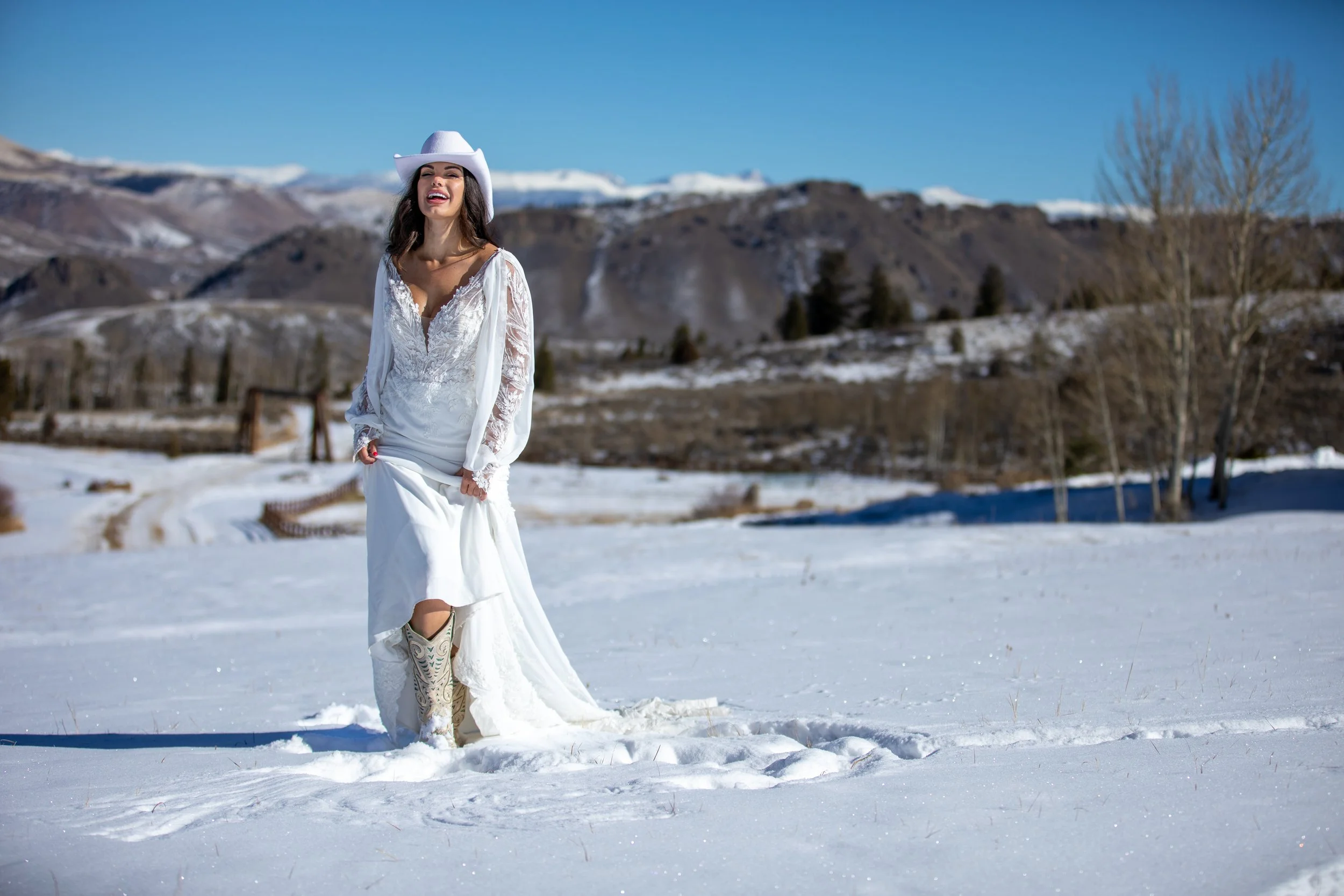 Bride in a lace gown with a long train walking across snow toward mountains in Hot Sulphur Springs, Colorado