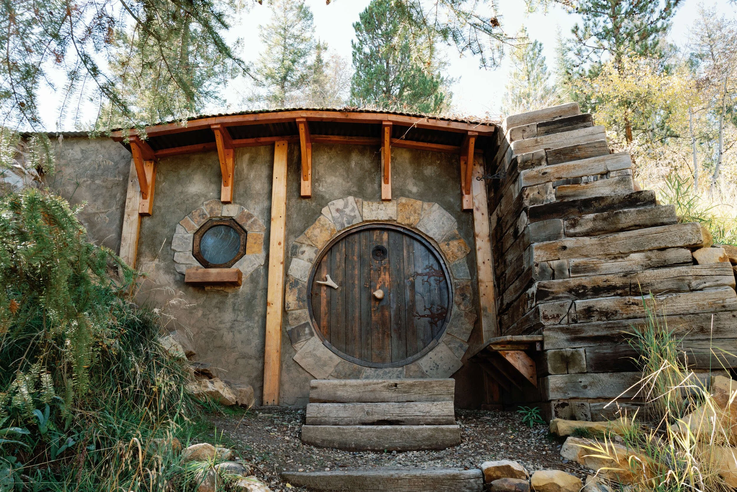 Sod-roofed Hobbit Hole with a round door and timber stairs climbing the hillside in Hot Sulphur Springs, Colorado