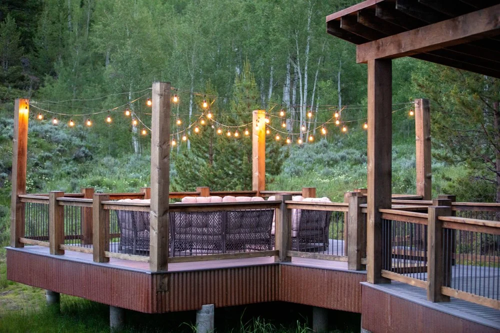Wooden deck strung with café lights beside pine trees at Tundra Springs, Colorado mountain wedding venue