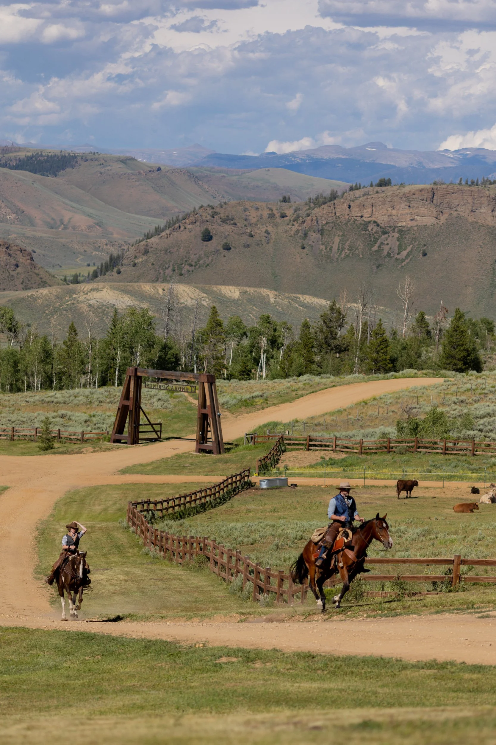 Two riders on horseback on a meadow trail with mountain ridges behind at Tundra Springs, Colorado mountain wedding venue