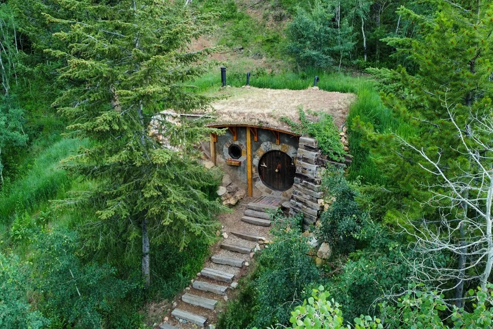 Hobbit Hole with a round wooden door and stone path tucked into pine forest in Hot Sulphur Springs, Colorado