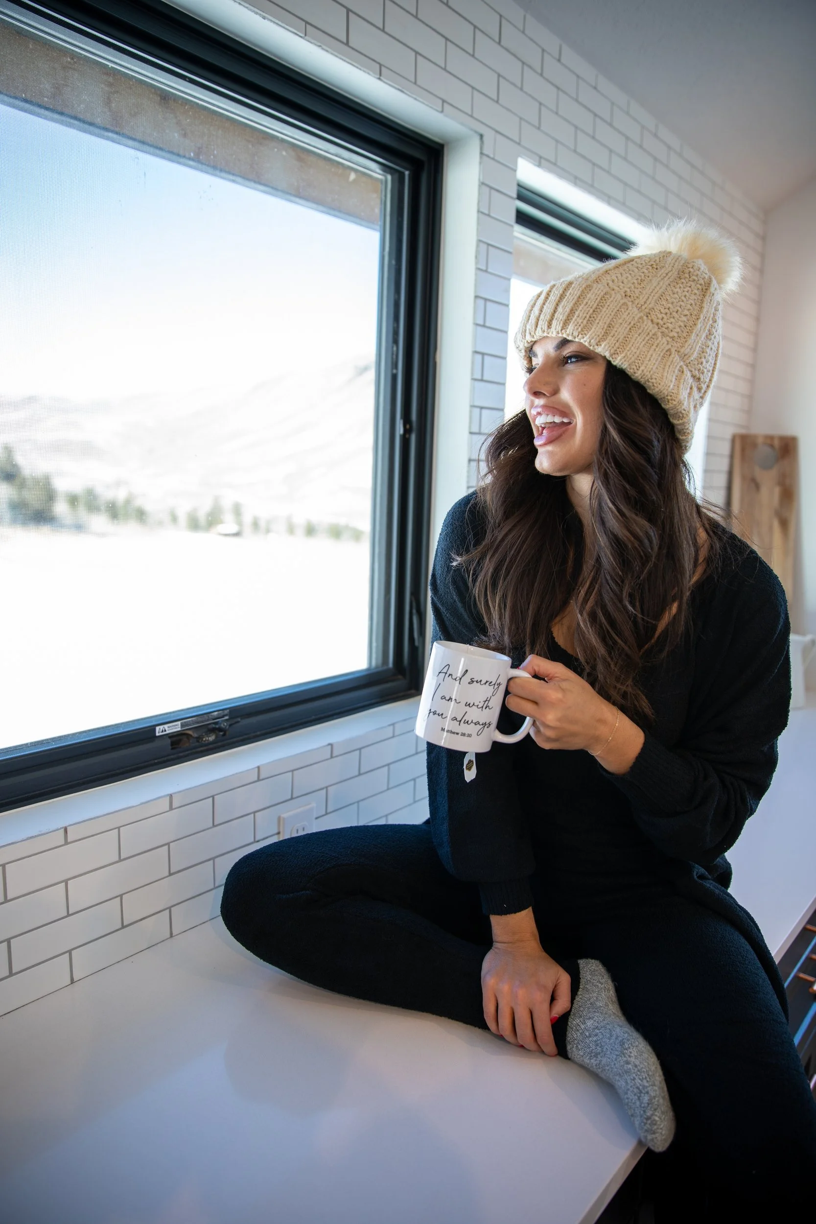 Woman in a knit beanie holding a mug by a bright window at Tundra Springs, Colorado mountain wedding venue
