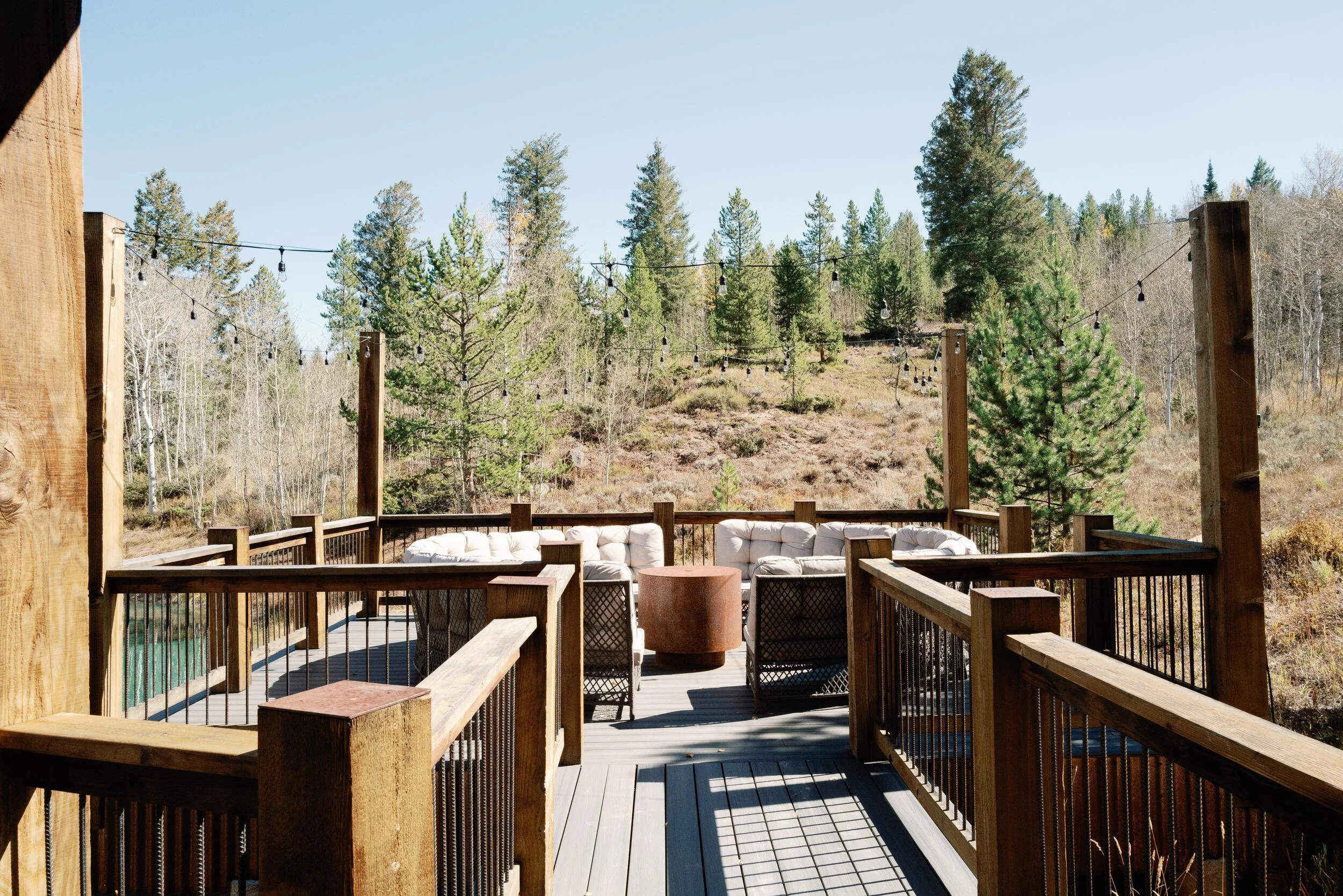 Wood-railed deck with outdoor seating and pine trees beyond, in Hot Sulphur Springs, Colorado