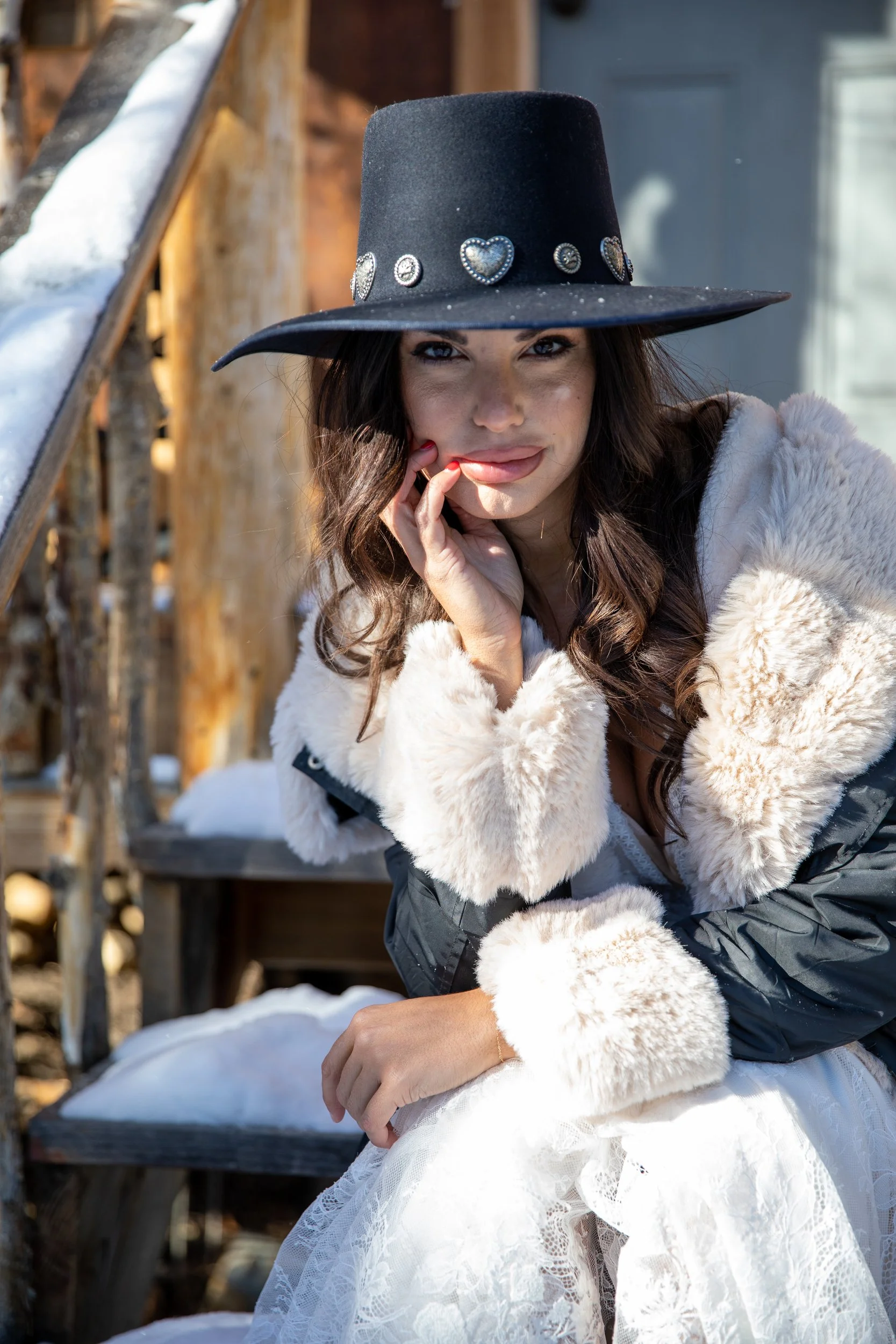 Bride in a black wide-brim hat and white fur wrap against a log wall at Tundra Springs, Colorado mountain wedding venue