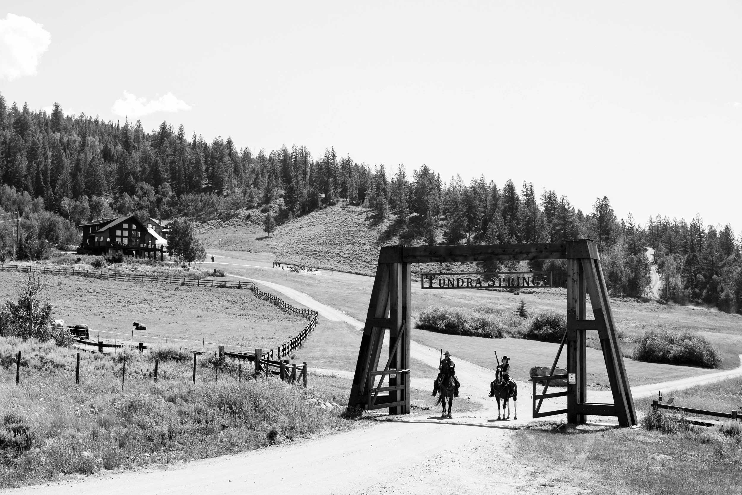 Black-and-white view of the Tundra Springs entrance gate with two riders on horseback in Hot Sulphur Springs, Colorado