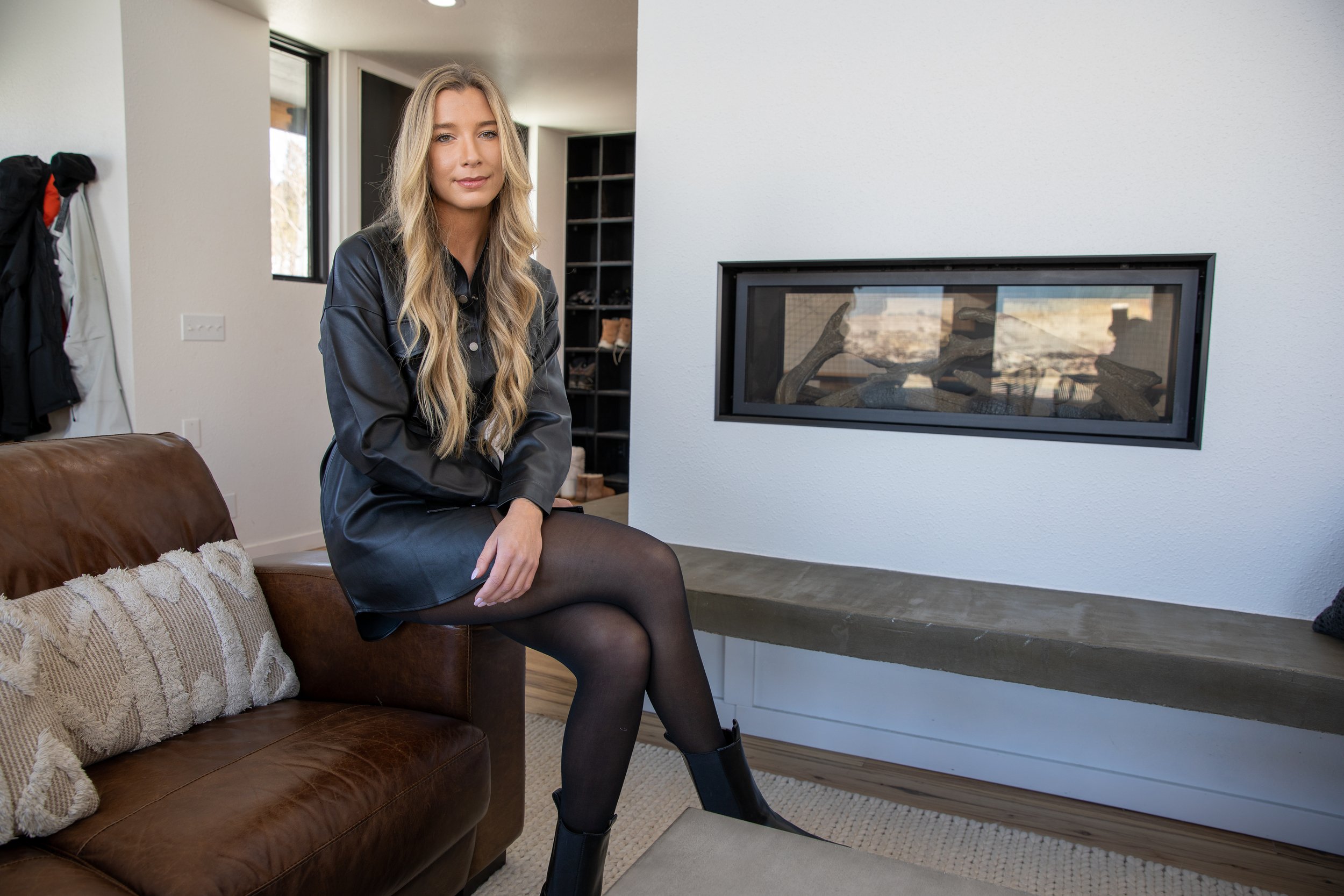 Woman with long blonde hair seated on a leather sofa beside a fireplace in a mountain lodge in Hot Sulphur Springs, Colorado