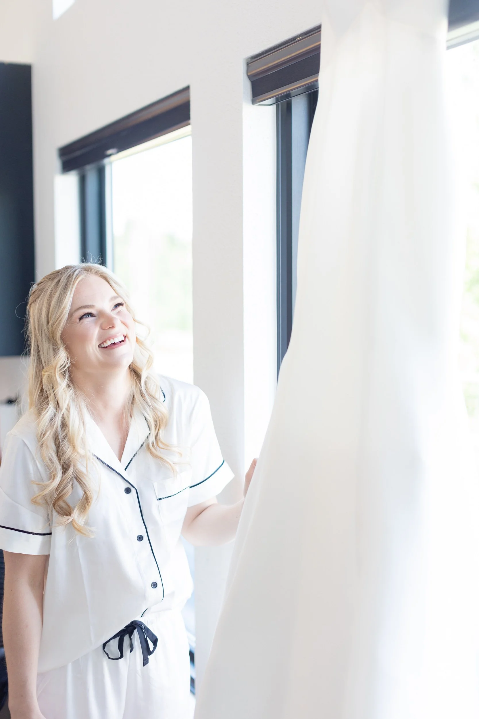 Bride in a white robe by a window and sheer curtain while getting ready at Tundra Springs, Colorado mountain wedding venue