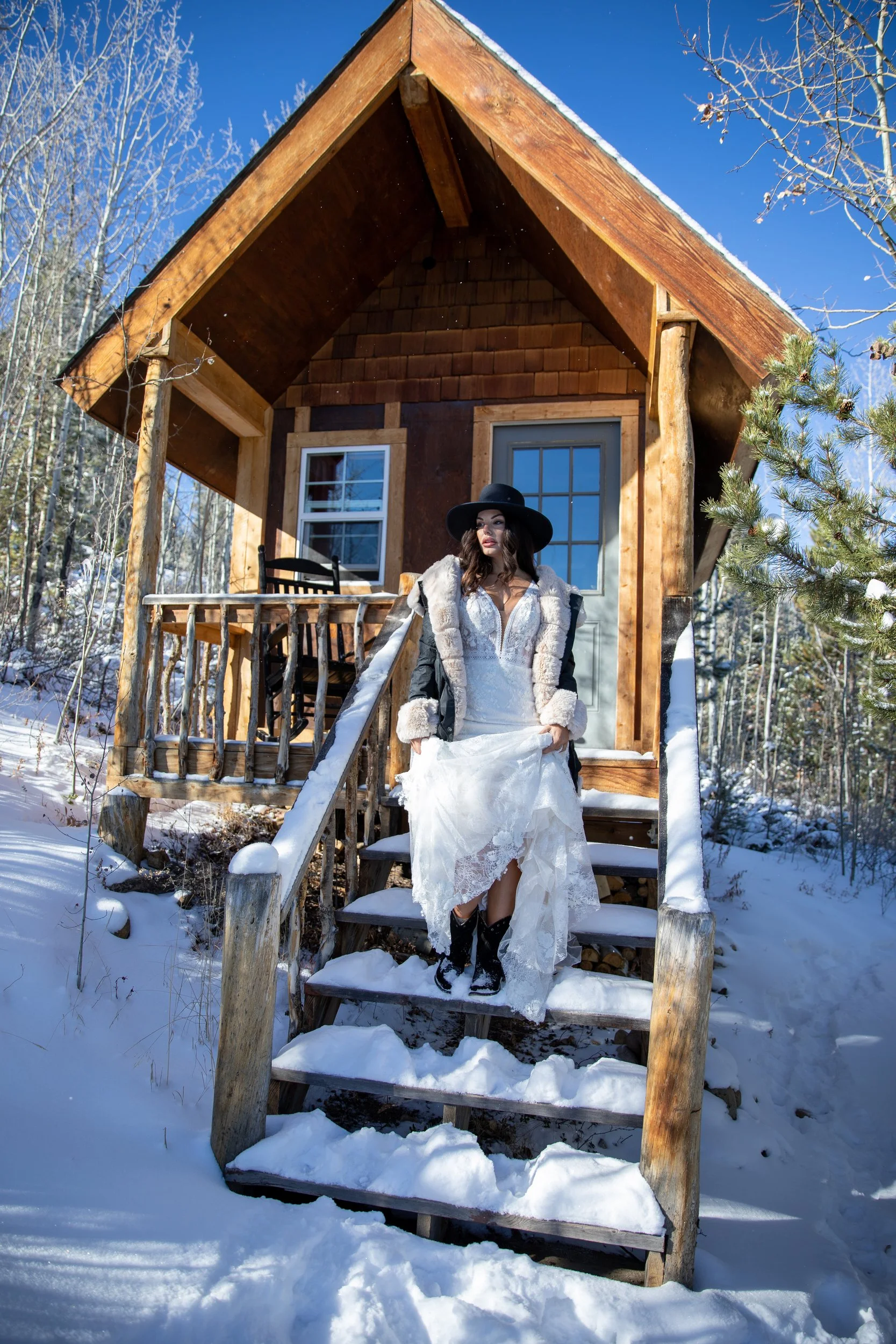 Bride in a white gown on the steps of a log cabin in snow at Tundra Springs, Colorado mountain wedding venue