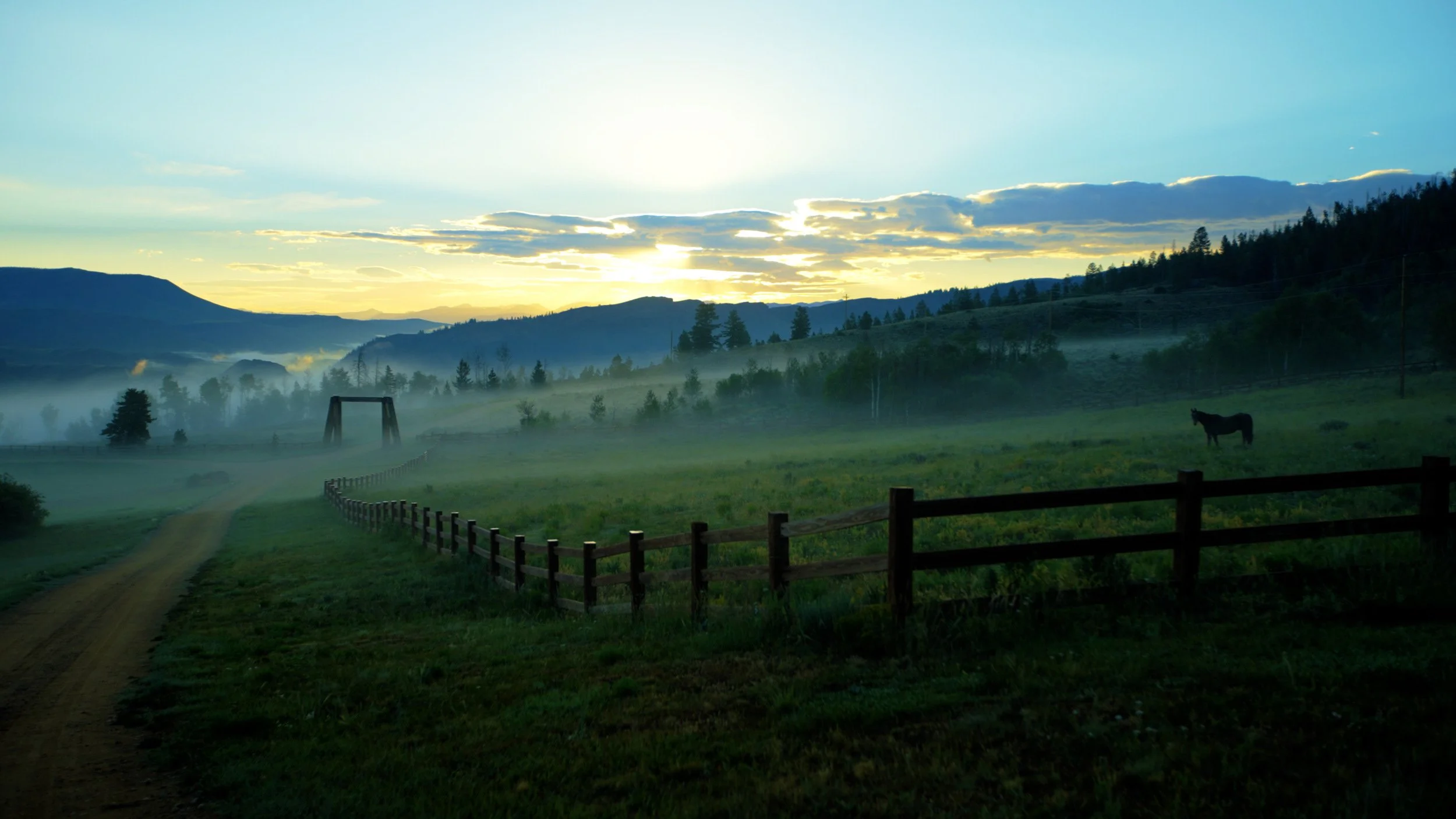 Misty sunrise over a fenced pasture with distant mountains in Hot Sulphur Springs, Colorado