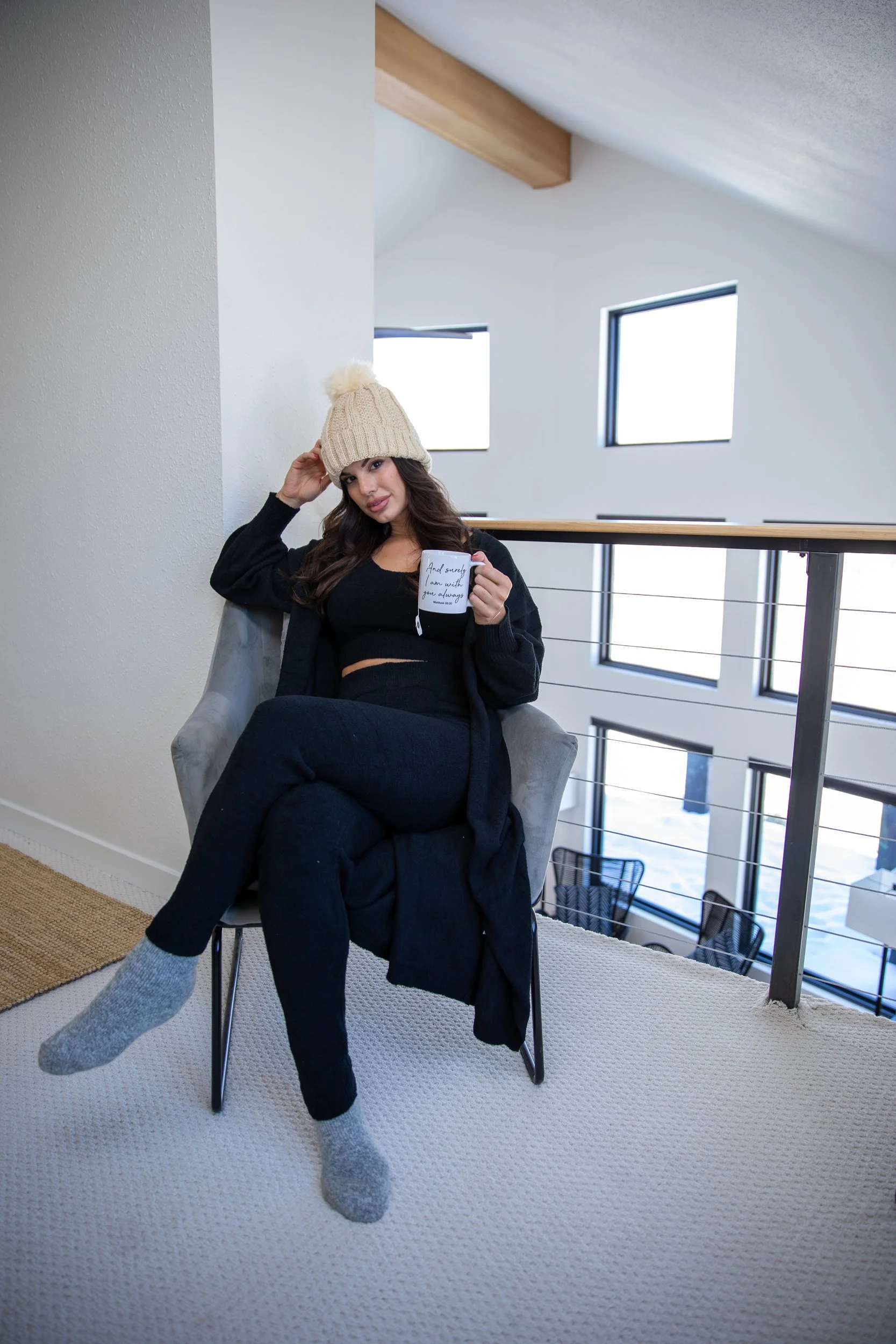 Woman in a beanie seated on a loft chair beside a wood railing in a modern cabin in Hot Sulphur Springs, Colorado