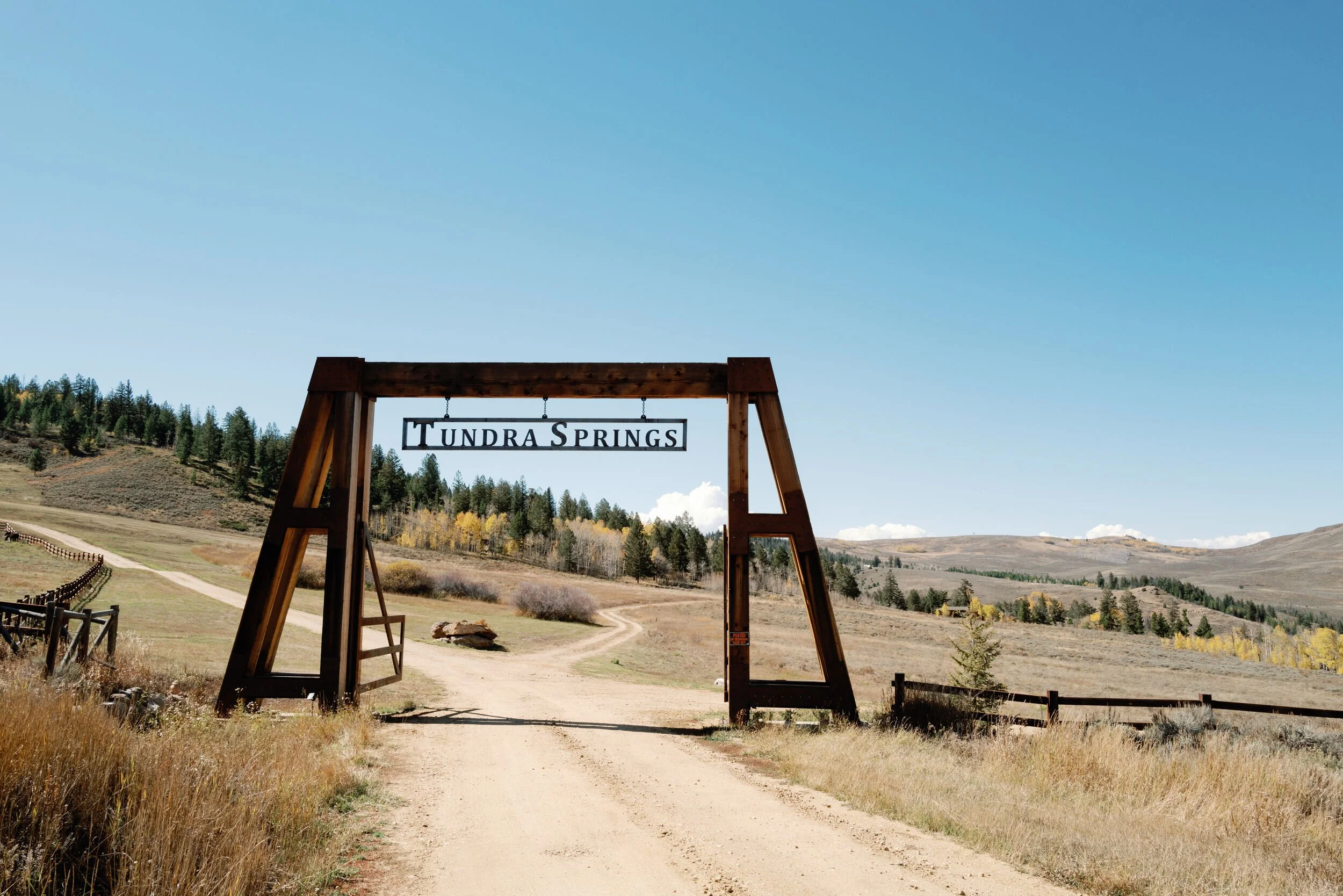 Wooden entrance gate with a Tundra Springs sign over a dirt road with mountains beyond in Hot Sulphur Springs, Colorado